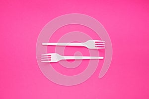 Two white plastic forks on a pink background