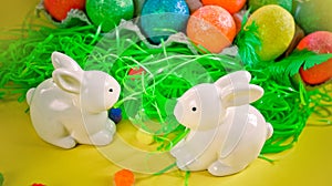 Two white porctlain rabbits near colorful bright eggs