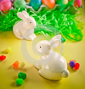 Two white porctlain rabbits near colorful bright eggs