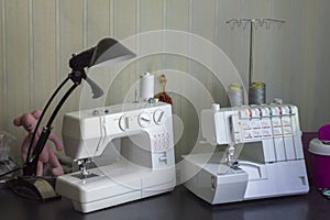 Two white sewing machines with threads and a black lamp on the table