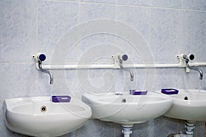 Two white sinks and liquid soap in public toilet.