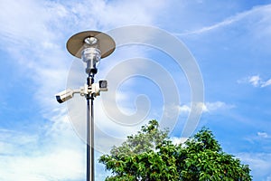 Two white surveillance cameras on the metal lamp post on blue sky background in public park