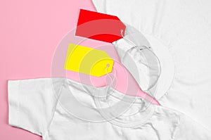 Two white T-shirts on a pink background with blank price tags. Blank label on clothes