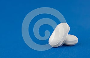 Two white tablets close-up on a blue background. Medicine