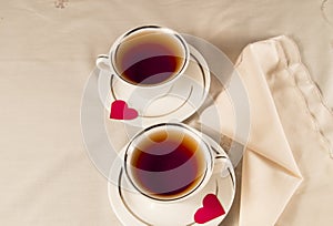 Two white tea cups on a saucer with red hearts