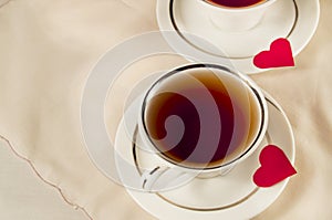 Two white tea cups on a saucer with red hearts