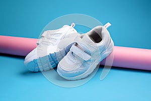 two white teen sneakers with velcro fasteners for comfortable footwear on a pink long paper roll on a blue background