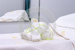 Two white towels rolled and fastened with green tape on massage table and mirror on the wall