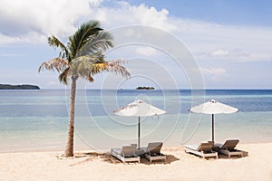 Two white umbrellas with chaise-lounges and palm tree on white sand beach