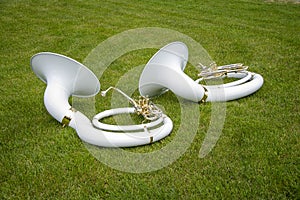 Two white wind musical instrument by a sousaphone-Helicon lying on the green grass in the Park. photo