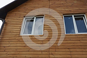 Two white windows on a brown wall of a house