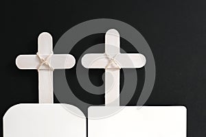 Two white wooden memorial cross with white ribbon in black background.