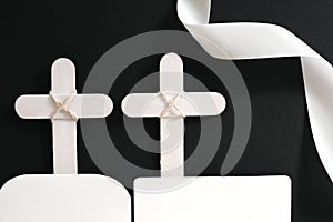 Two white wooden memorial cross with white ribbon in black background.