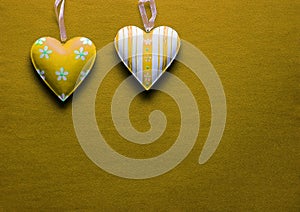 Two white and yellow metal hearts on a golden paper background
