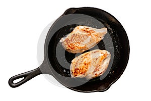 Two whole chicken breasts roasting in cast iron pan isolated on white. Top view