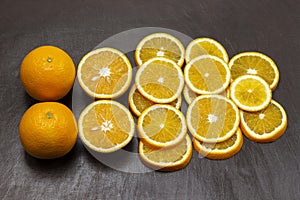 Two whole oranges, sliced orange on a brown background