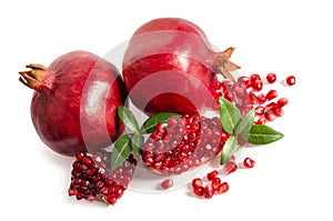 Two whole and part of a pomegranate with pomegranate seeds and leaves