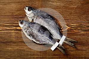 Two whole sun-dried breams with labelson tails on wooden background