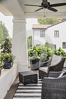 Two wicker chairs and pots of plants on the front porch of a historic craftsman house with blurred neighboring luxury home in back