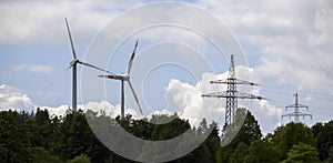 two wind turbines behind a wooded area and a power pole next to it