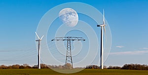 Two wind turbines in a field with the moon in the middle.