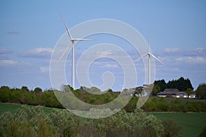 Two wind turbines over English countryside against blue sky with small clouds
