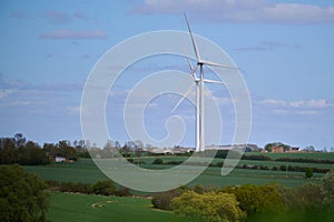 Two wind turbines over English countryside against blue sky with small clouds
