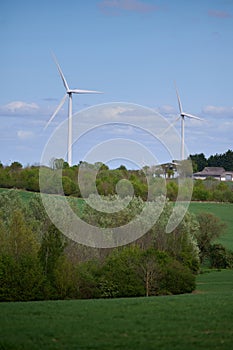 Two wind turbines over English countryside against blue sky with small clouds