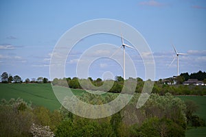 Two wind turbines over English countryside against blue sky with small clouds