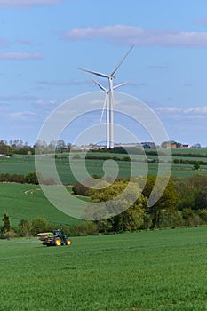 Two wind turbines over English countryside and a tractor against blue sky with small clouds