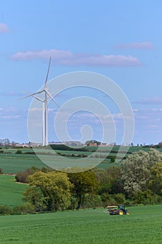 Two wind turbines over English countryside and a tractor against blue sky with small clouds