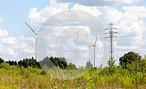 Two wind turbines and power lines in a green field, country landscape shot, sunny weather. Green energy, ecology