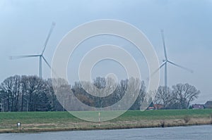 Two wind turbines rotate over trees