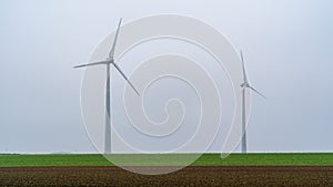 Two wind turbines stood in field on cold foggy winters day