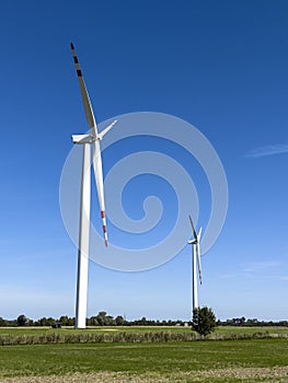 Two windmills producing renewable energy standing in a field.