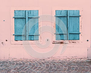 Two windows with closed blue wooden shutters on a old house with a pink wall