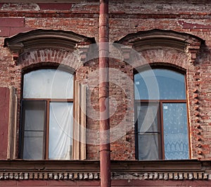 Two windows and drainpipe, on red brick wall