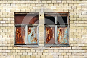 Two windows in the facade of an old abandoned building. Rusty metal sheets in a wooden frame window