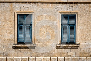 Two windows in old wall with closed shutters