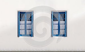 Two windows with open shutters on white wall. Greek island house front view