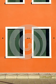 Two windows in orange wall with closed green shutters, Pellestrina island, Venetian lagoon, Italy