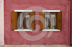 Two windows on a red wall from a colorful house of Burano island