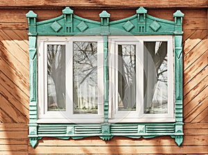 Two windows with shabby carved wooden architraves facade of 19th century wood house, Russia.