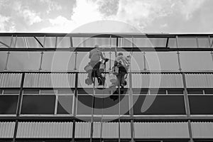 Two windows washers doing his job at high modern skyscraper with cloudy sky