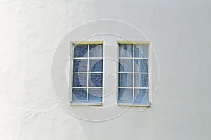 Two windows on the white wall of the house