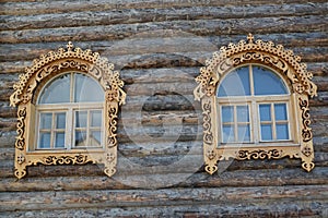 Two windows with wooden carved platbands on a timbered wall