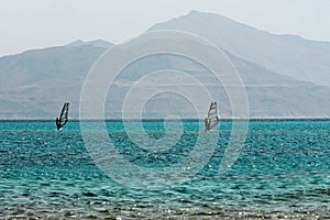 Two windsurfers, blue sea and mount background