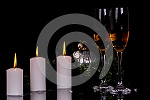 Two wine glasses with champagne, candles and Christmas ornaments on a black background