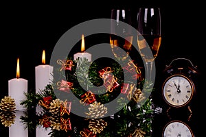 Two wine glasses with champagne, candles, clock, Christmas ornaments on a black background
