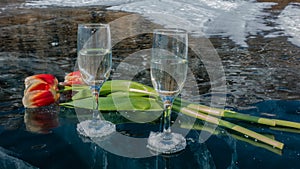 Two wine glasses with champagne sit on smooth, shiny blue ice.